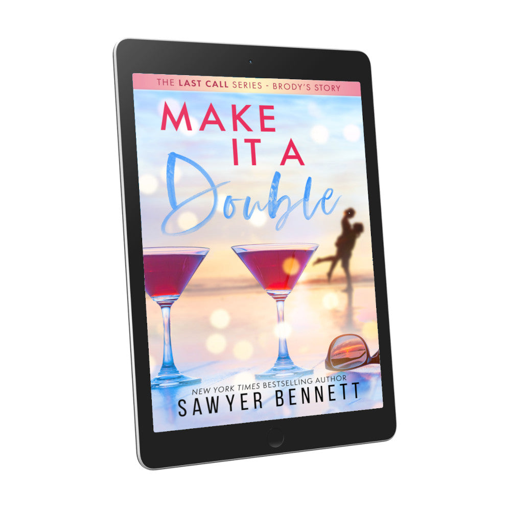 Contemporary romance book cover featuring a couple embracing on the beach in the background, with two martini glasses with pink liquid in the forefront, displayed on an e-reader. The title of the book is Make It a Double by New York Times Bestselling Author Sawyer Bennett.