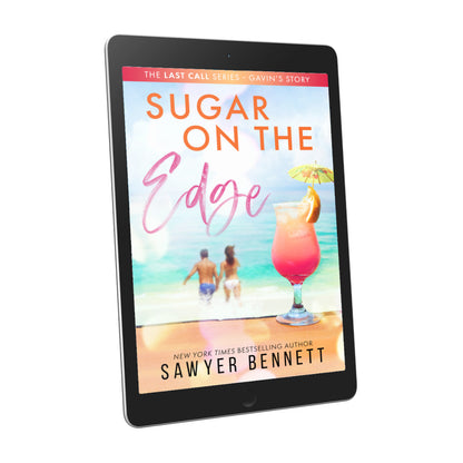 Contemporary romance book cover featuring a couple embracing on the beach in the background, with a hurricane glass with pink liquid and a drink umbrella in the forefront, displayed on an e-reader. The title of the book is Sugar on the Edge by New York Times Bestselling Author Sawyer Bennett.