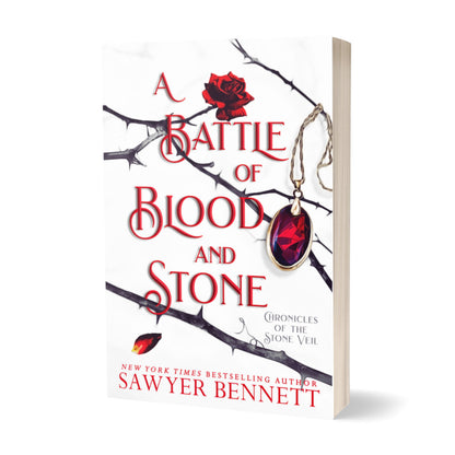 Fantasy romance paperback with thorned branches sprawled across a white background and blood red amulet hanging from one of the branches. The title of the book is A Battle of Blood and Stone by New York Times Bestselling Author Sawyer Bennett.