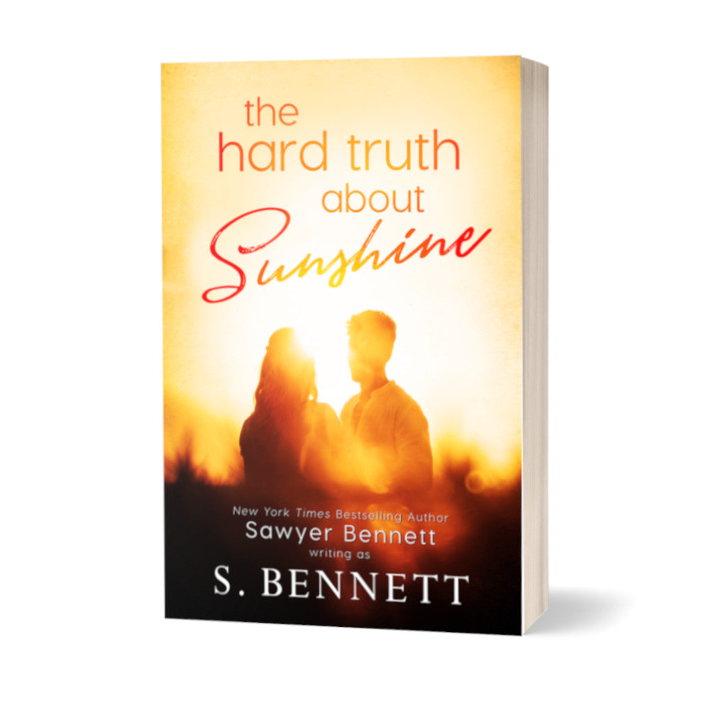 A general fiction paperback featuring a couple embracing in the glow of the sunshine, the background blurred and shades of yellow and orange. The title of the book is The Hard Truth About Sunshine by New York Times Bestselling Author Sawyer Bennett.