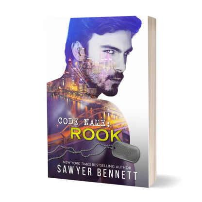 Romantic suspense paperback featuring an attractive man and city scape. The title of the book is Code Name: Rook by New York Times Bestselling Author Sawyer Bennett.